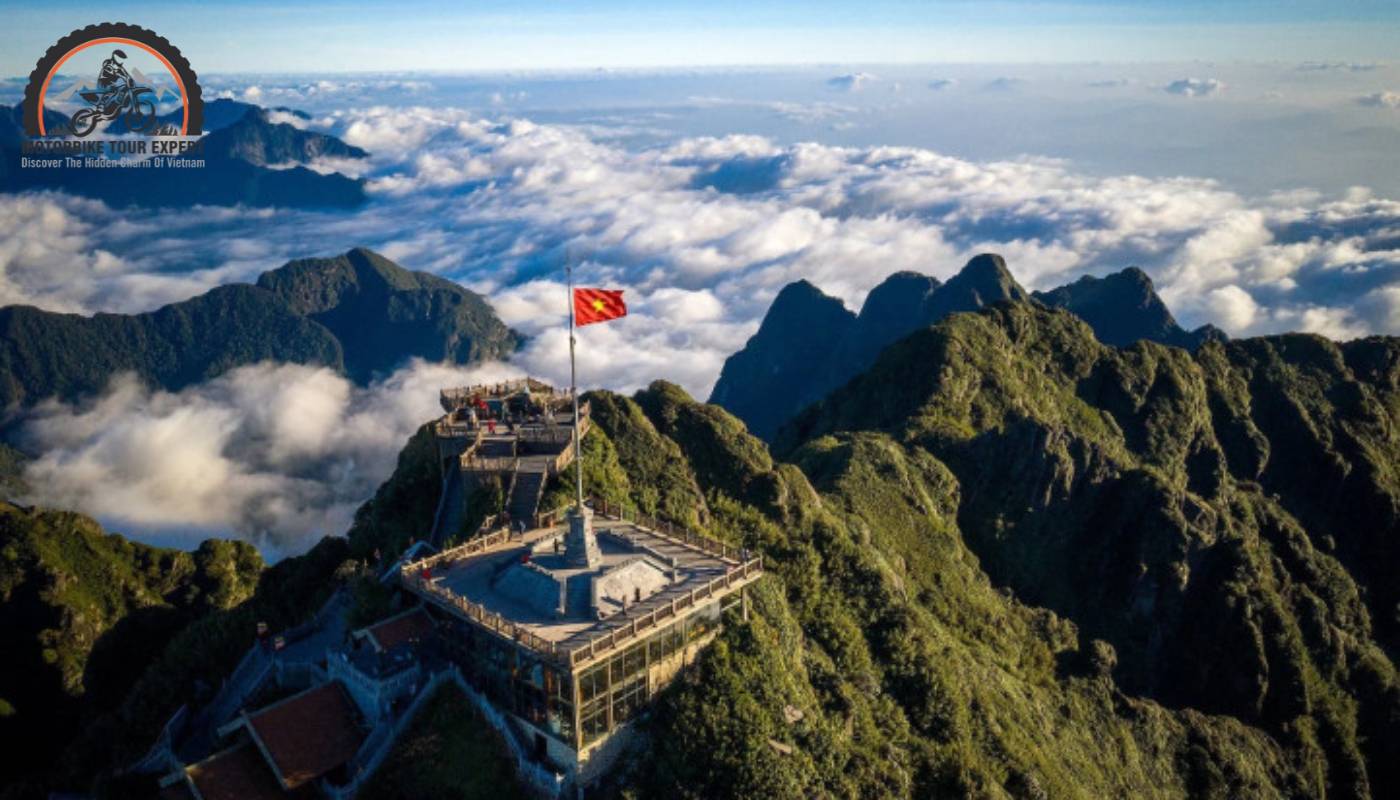 The peak of Fansipan Mountain reaching up into the blue sky, surrounded by billowing clouds