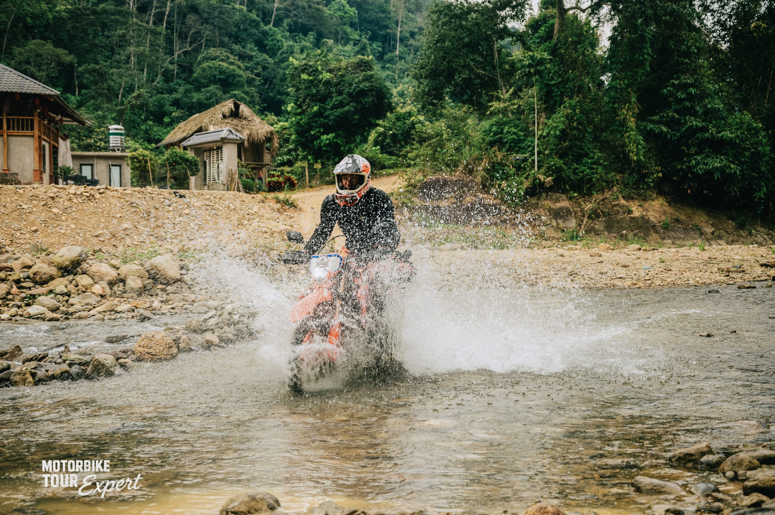 Motorbike rider crossing a stream on a rural route in Northern Vietnam during the wet season.