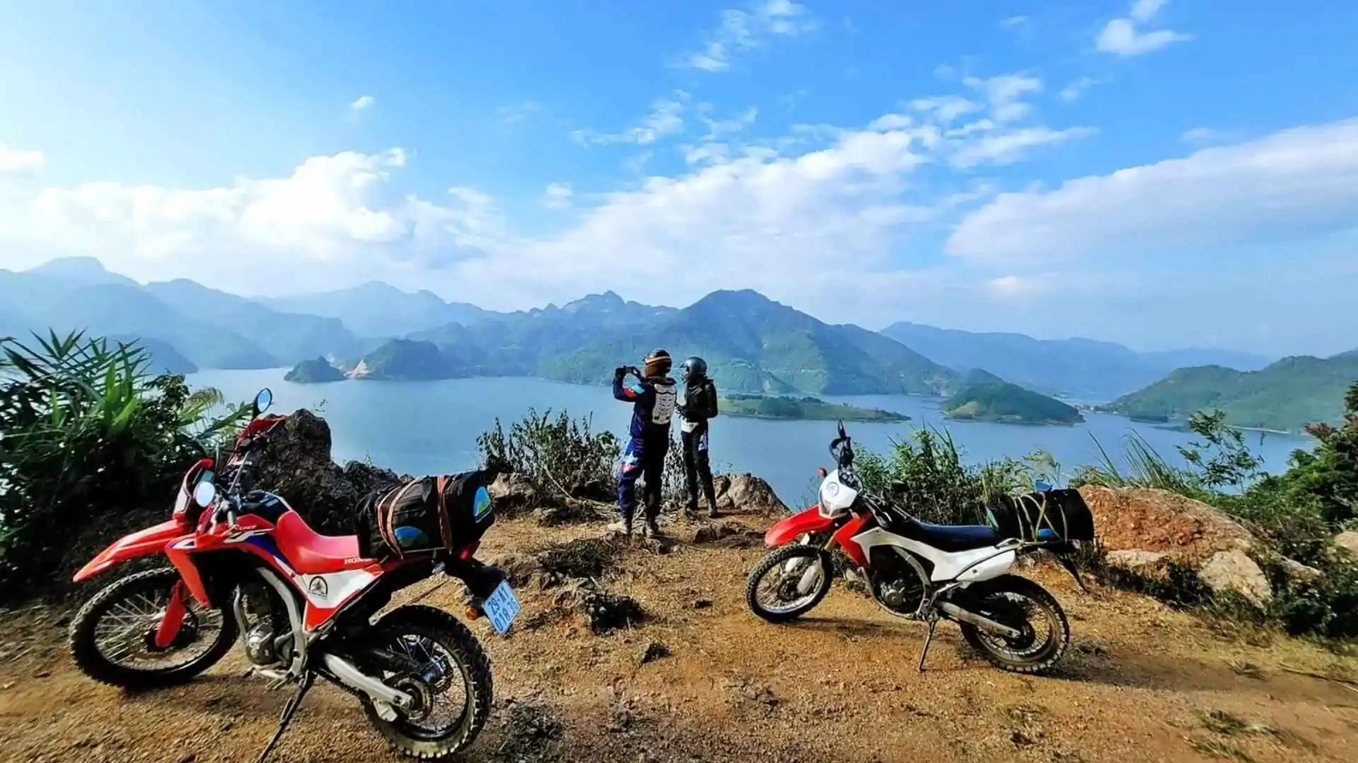 Two dirt bikes parked beside a lake surrounded by mountains in Northern Vietnam.